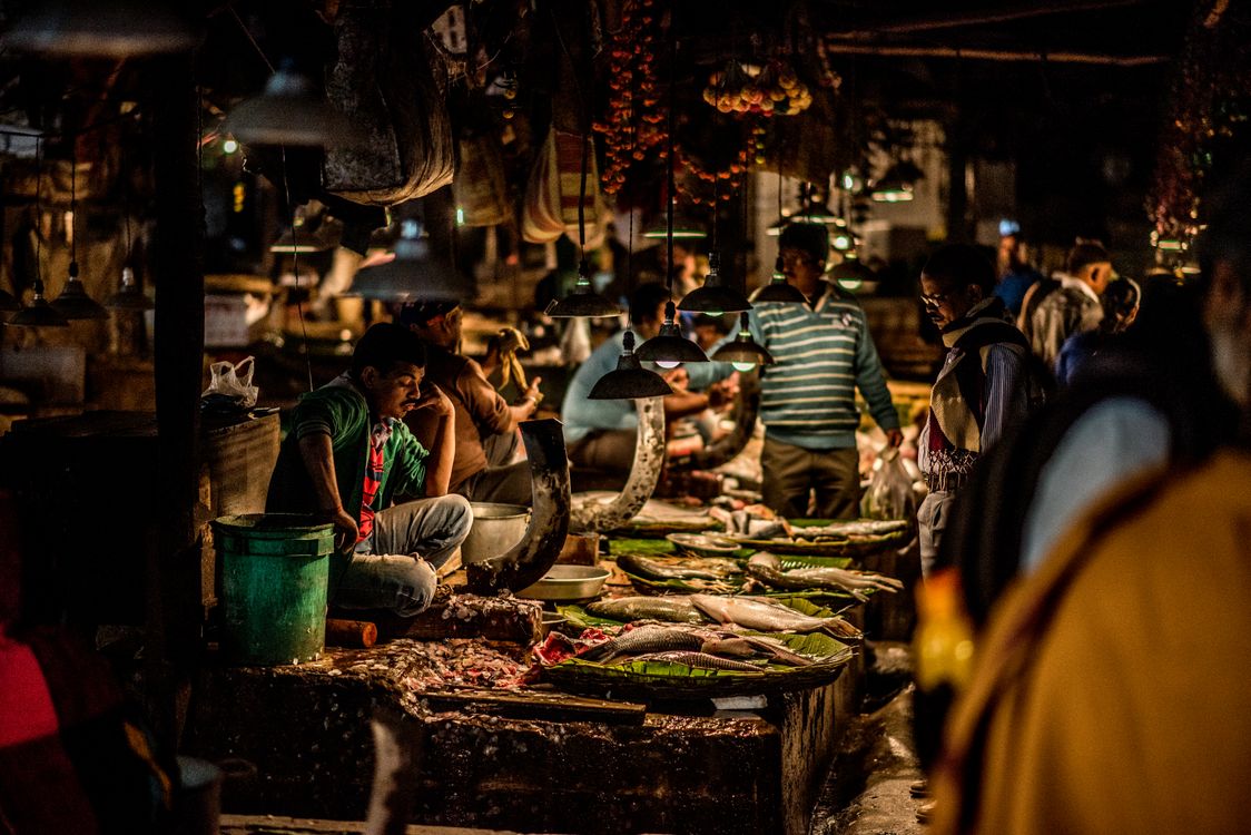 Free Vibrant night scene at an Indian fish market with vendors and customers bustling under warm lights. Stock Photo