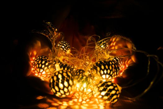Close-up of hands holding glowing string lights, casting warm shadows in darkness.