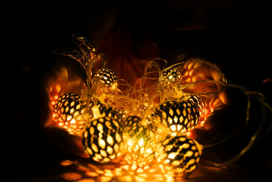 Close-up of hands holding glowing string lights, casting warm shadows in darkness.