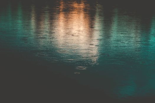 Calm water surface reflecting lights with gentle raindrops creating subtle ripples.