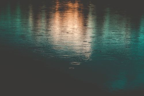 Free Calm water surface reflecting lights with gentle raindrops creating subtle ripples. Stock Photo