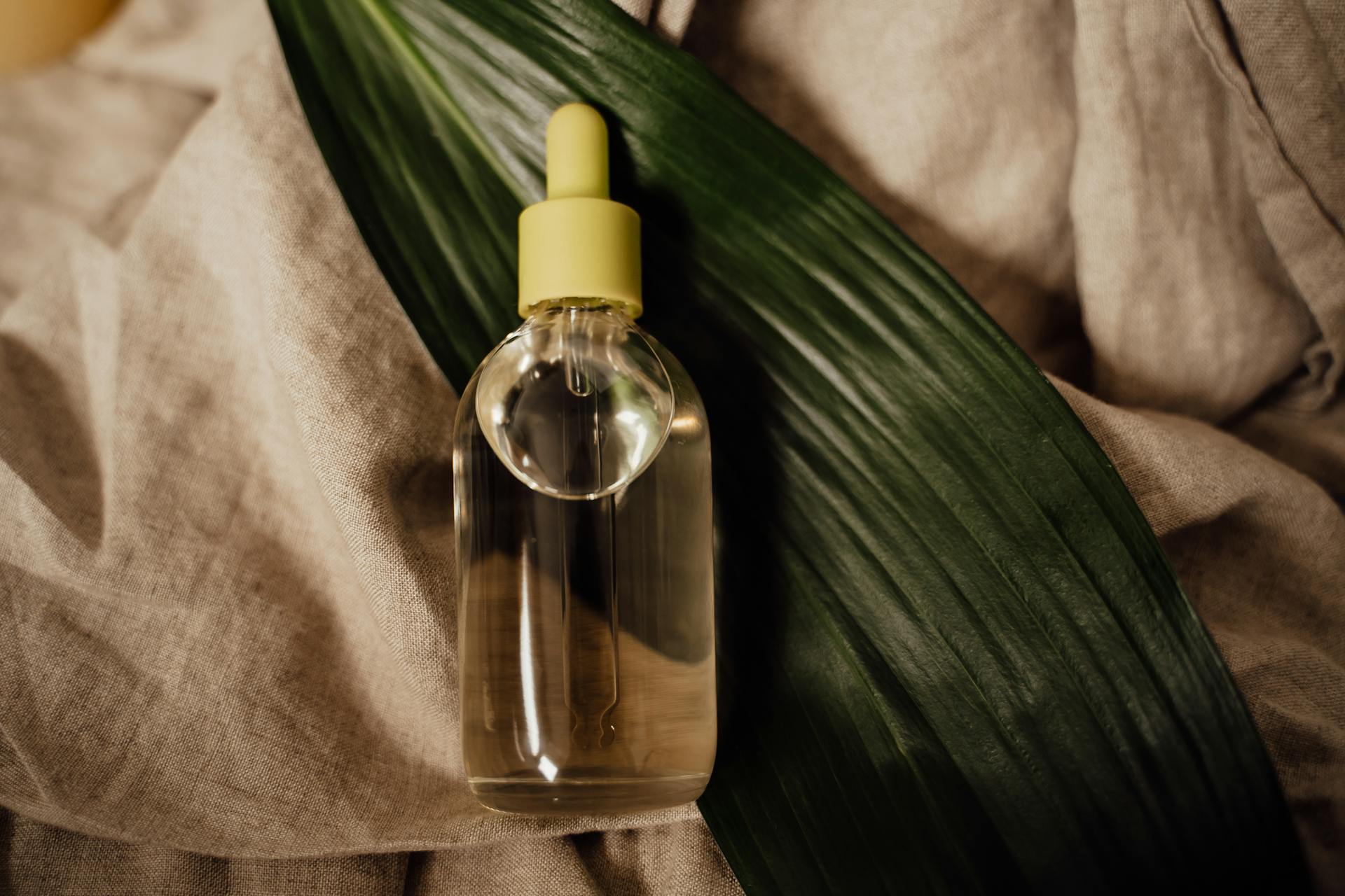 Close-up of a glass dropper bottle filled with essential oil, placed on linen fabric with a leaf.