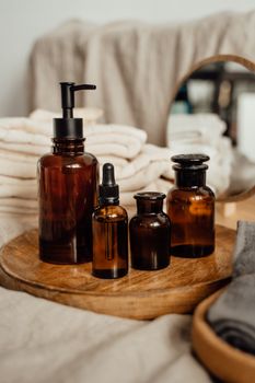 Serene still life of skincare products in glass bottles on a wooden tray with soft towels.