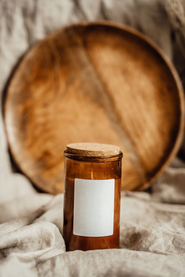 Amber candle jar with a cork lid against a wooden round — Alesia Kozik on Pexels