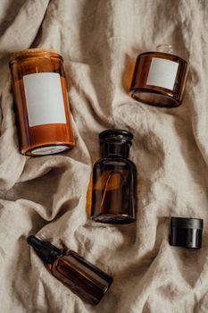 Assorted glass bottles for cosmetics on a beige linen cloth, emphasizing sustainability.