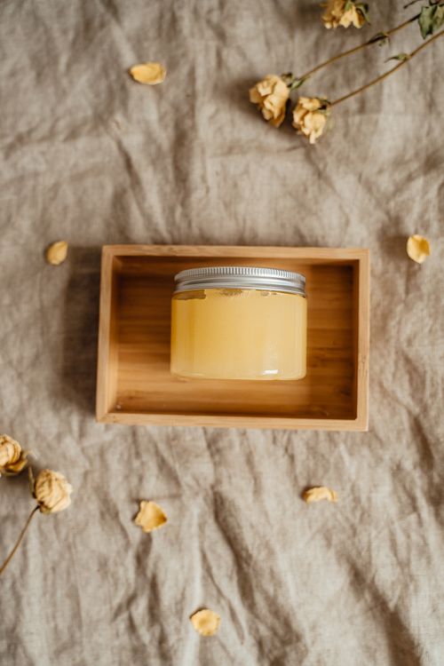 Free A glass jar of yellow skincare product displayed in a wooden box with dried flowers. Stock Photo