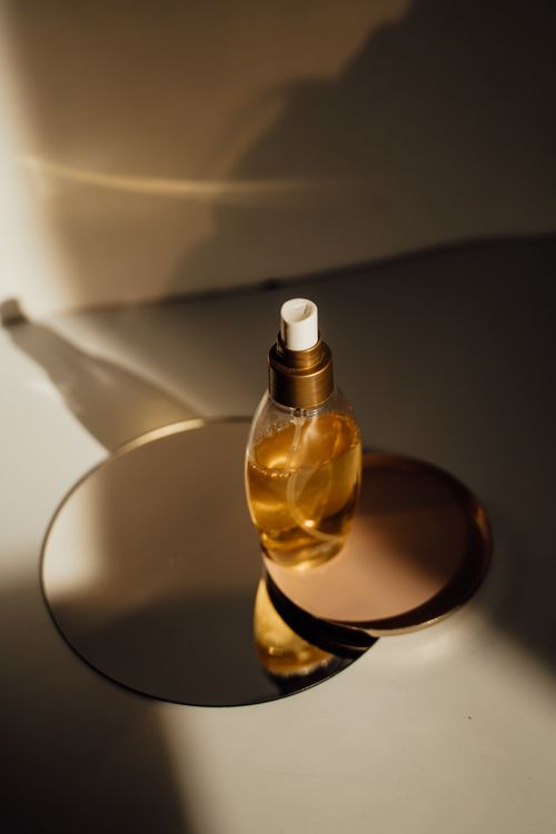 Free A stylish glass perfume bottle with shadows on a mirror under warm lighting. Stock Photo