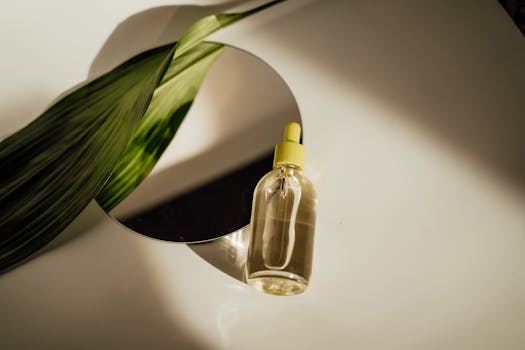 A minimalist image showcasing a clear cosmetic serum bottle beside a green leaf on a round mirror.