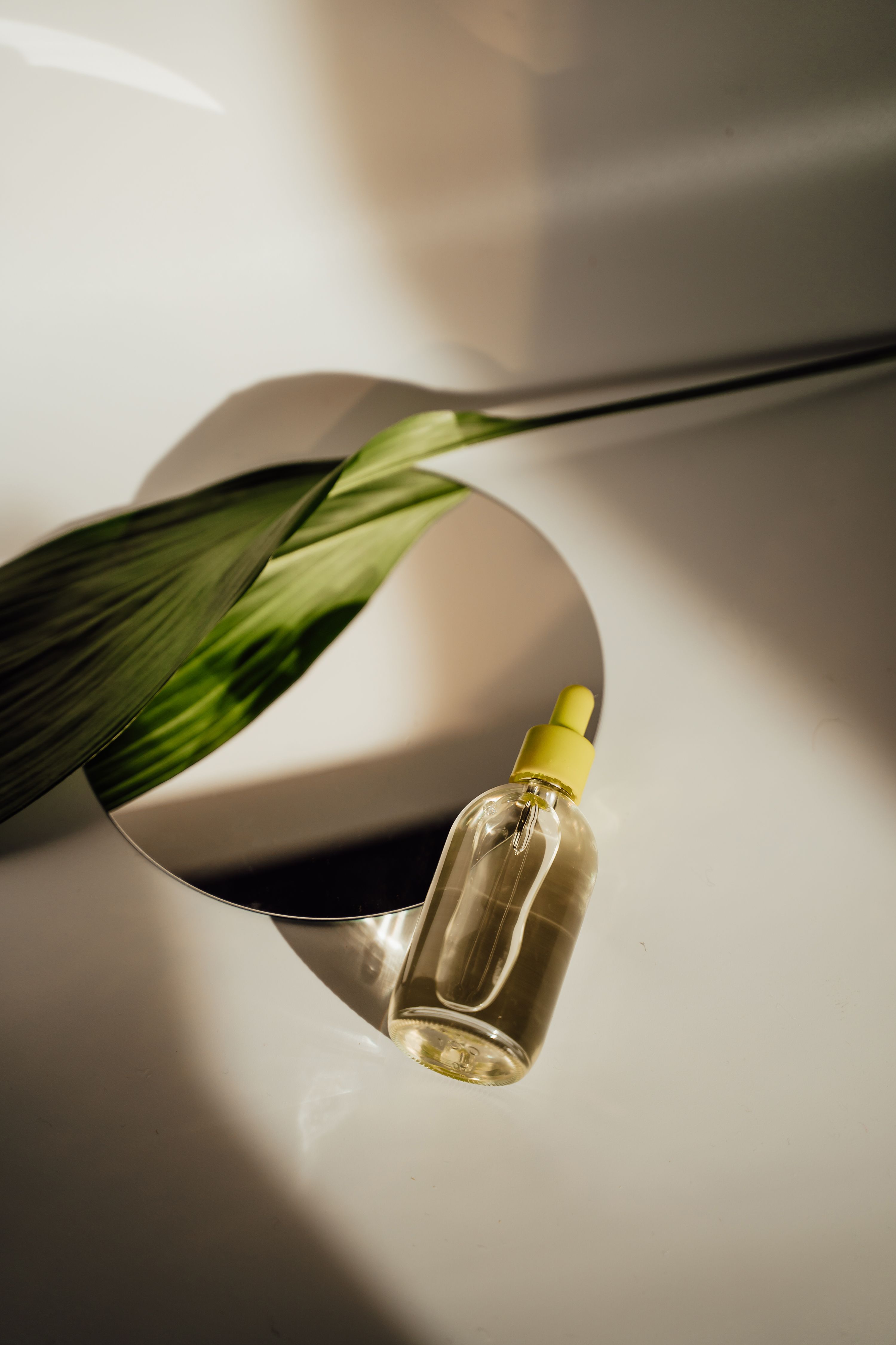 Skincare serum bottle with a leaf reflection on a neutral surface