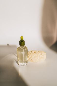 Glass bottle of skincare oil with dropper and natural sponge on a minimalistic setup.