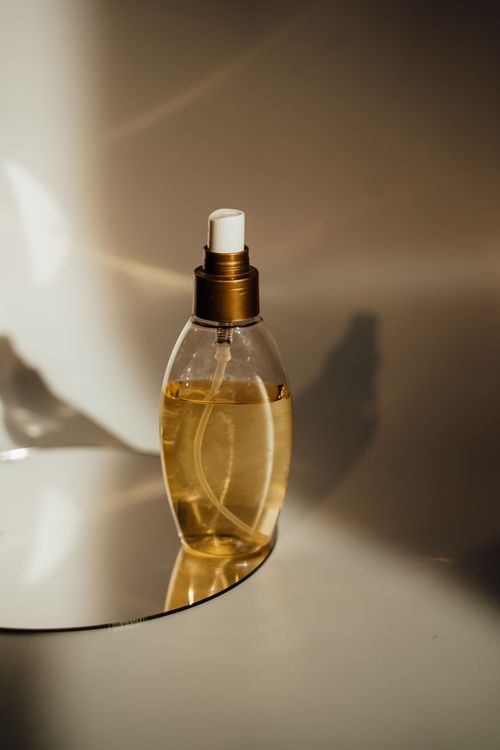 Free Close-up of a perfume bottle elegantly placed on a reflective surface with warm lighting. Stock Photo