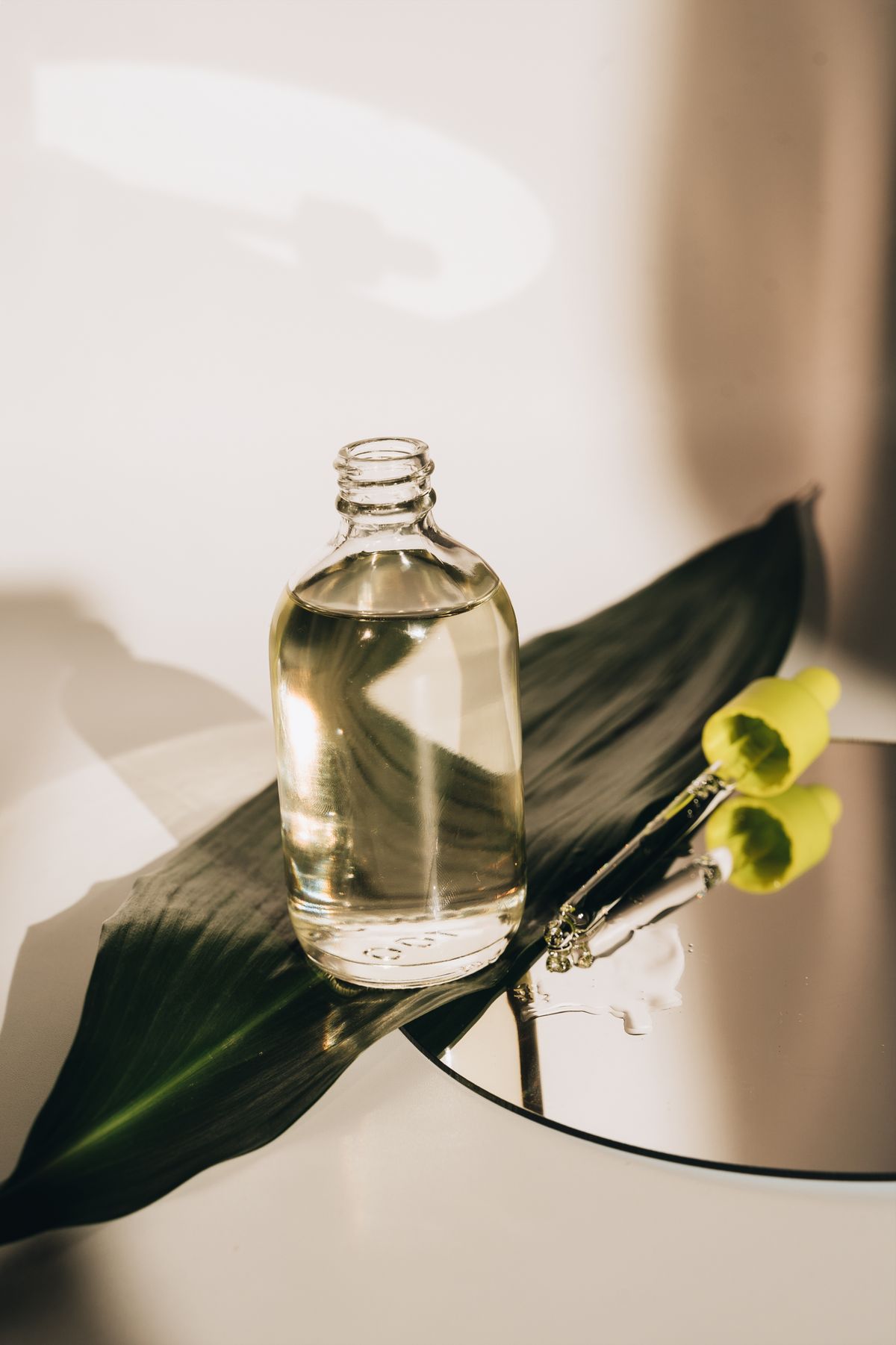 Clear glass scent bottle resting on a green leaf in soft daylight — Verde Assoluto