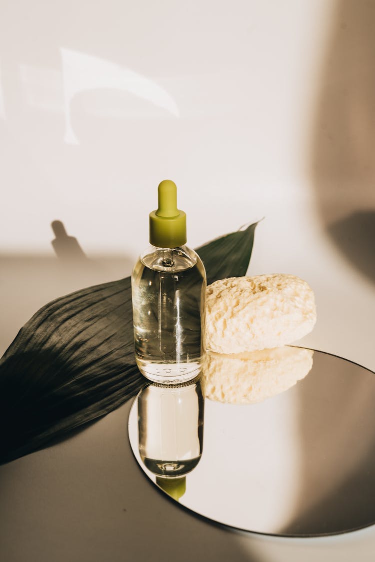 Clear Glass Bottle With Dropper On A Round Mirror