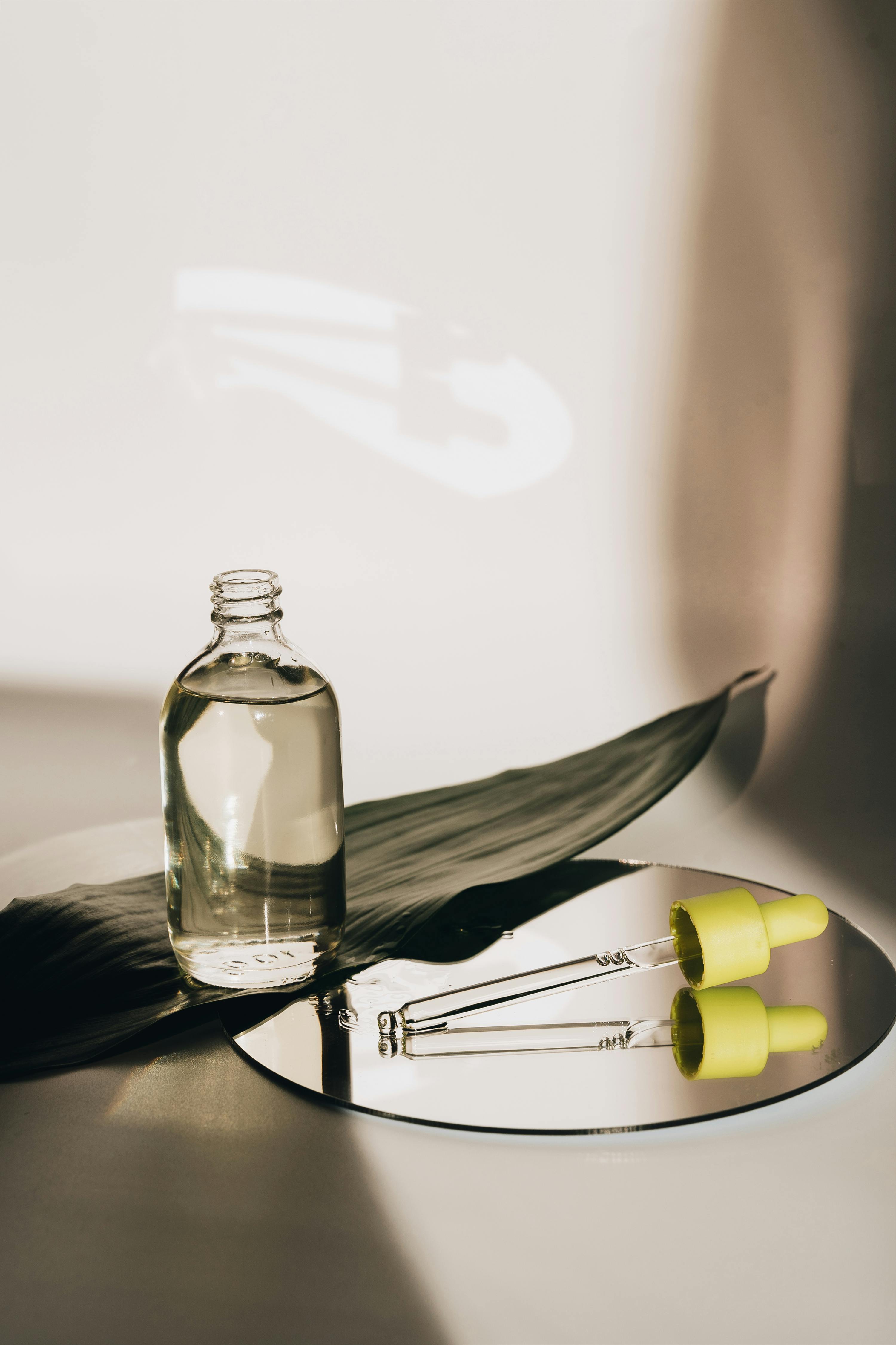 An image of a bottle with oil and a pipette lying on a mirror 