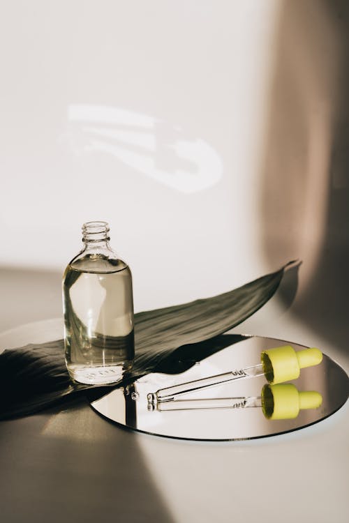 An image of a bottle with oil and a pipette lying on a mirror