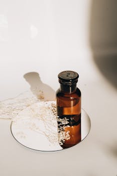Stylish minimalistic photo of a glass bottle with dried flowers on a reflective surface.