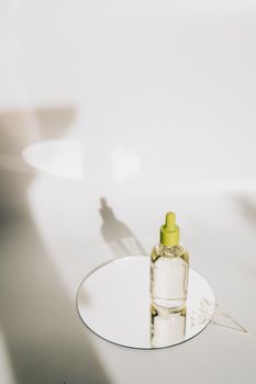 A minimalist close-up of a skincare dropper bottle on a reflective surface with elegant shadows.