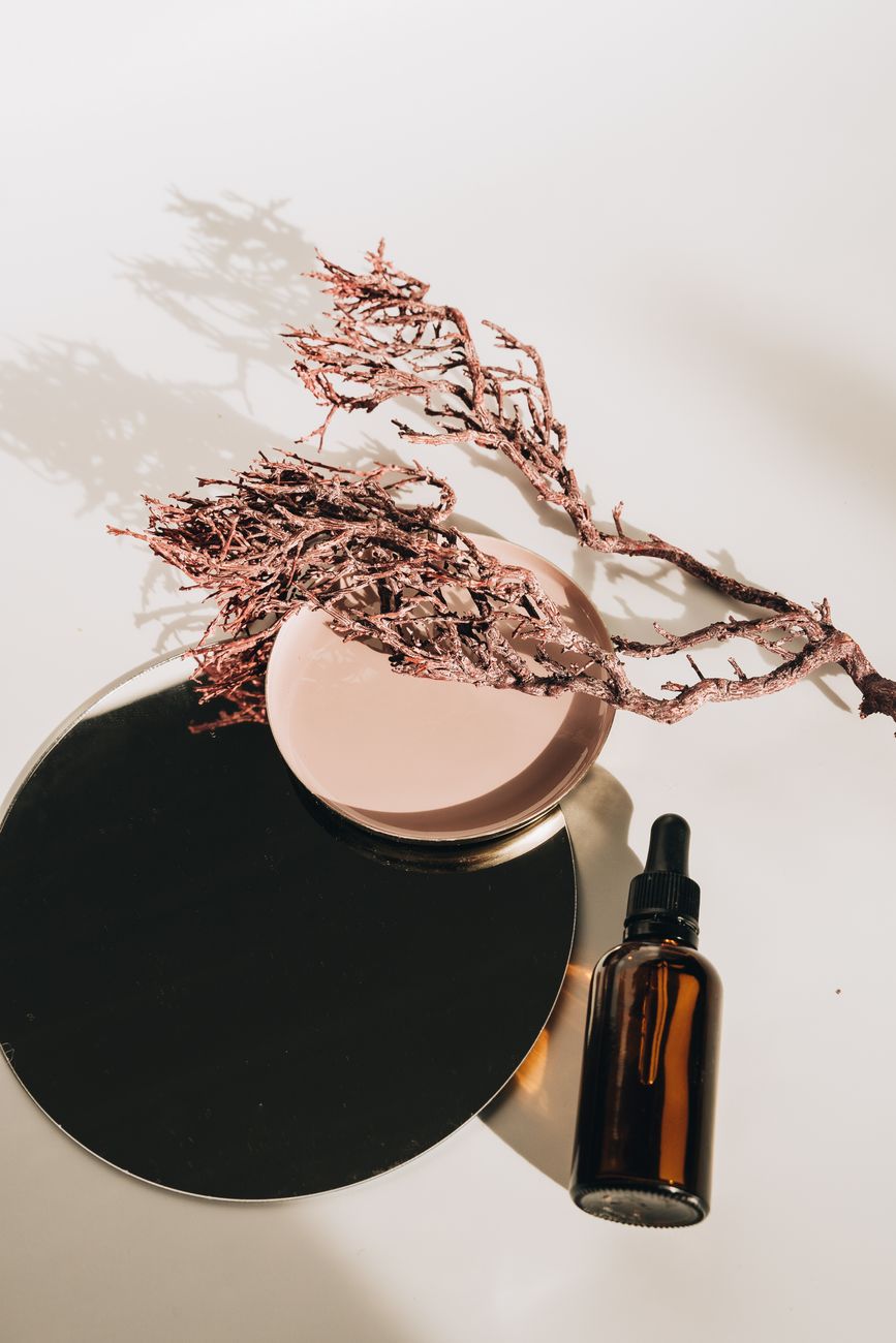 Aesthetic arrangement of a glass serum bottle with natural twigs and a plate, perfect for skincare branding.