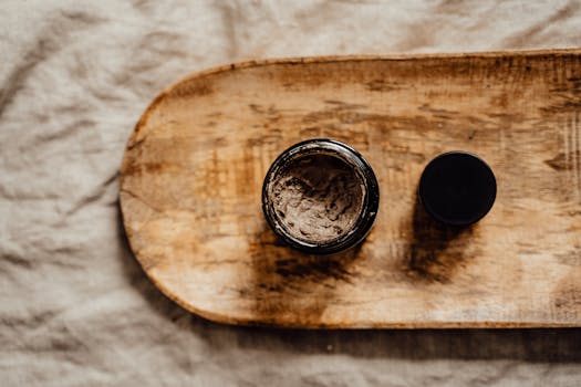 Top view of an open jar with skincare product on a rustic wooden tray, warm tones.
