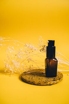 A sleek brown pump bottle on a cork base with a vibrant yellow background and delicate dried flowers.