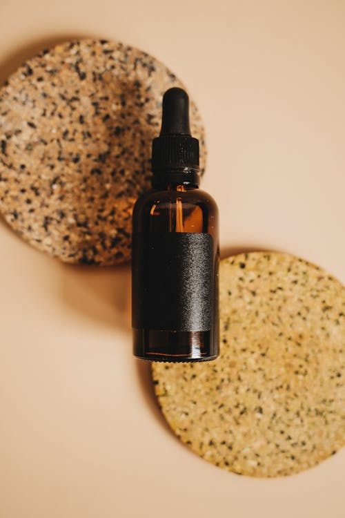 Brown Glass Bottle With Black Dropper on Round Cork Coasters