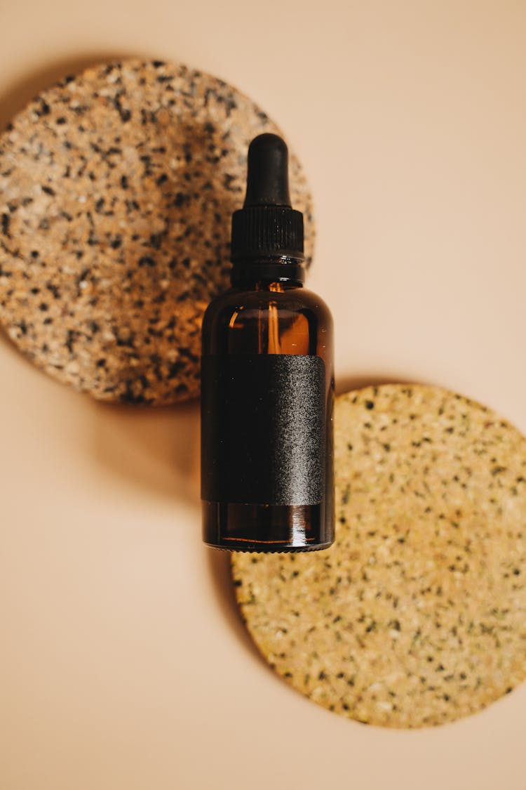 Brown Glass Bottle With Black Dropper On Round Cork Coasters