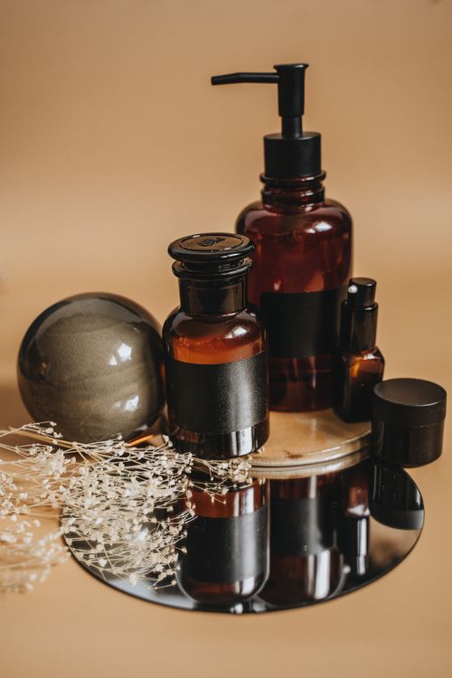 Free Sophisticated display of amber bottles and delicate flowers on a reflective surface, ideal for product branding. Stock Photo
