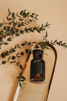 Elegant flatlay of a cosmetic bottle with greenery on a beige background.