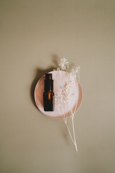 Minimalist top view of a skincare bottle with dried flowers on a pale pink plate.