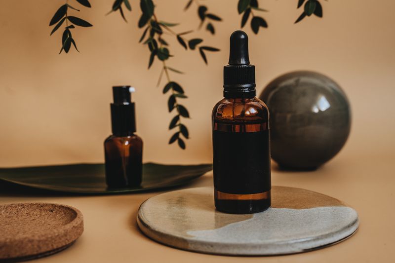 Elegant arrangement of amber dropper bottles with green leaves and earthy textures in a minimalist style.