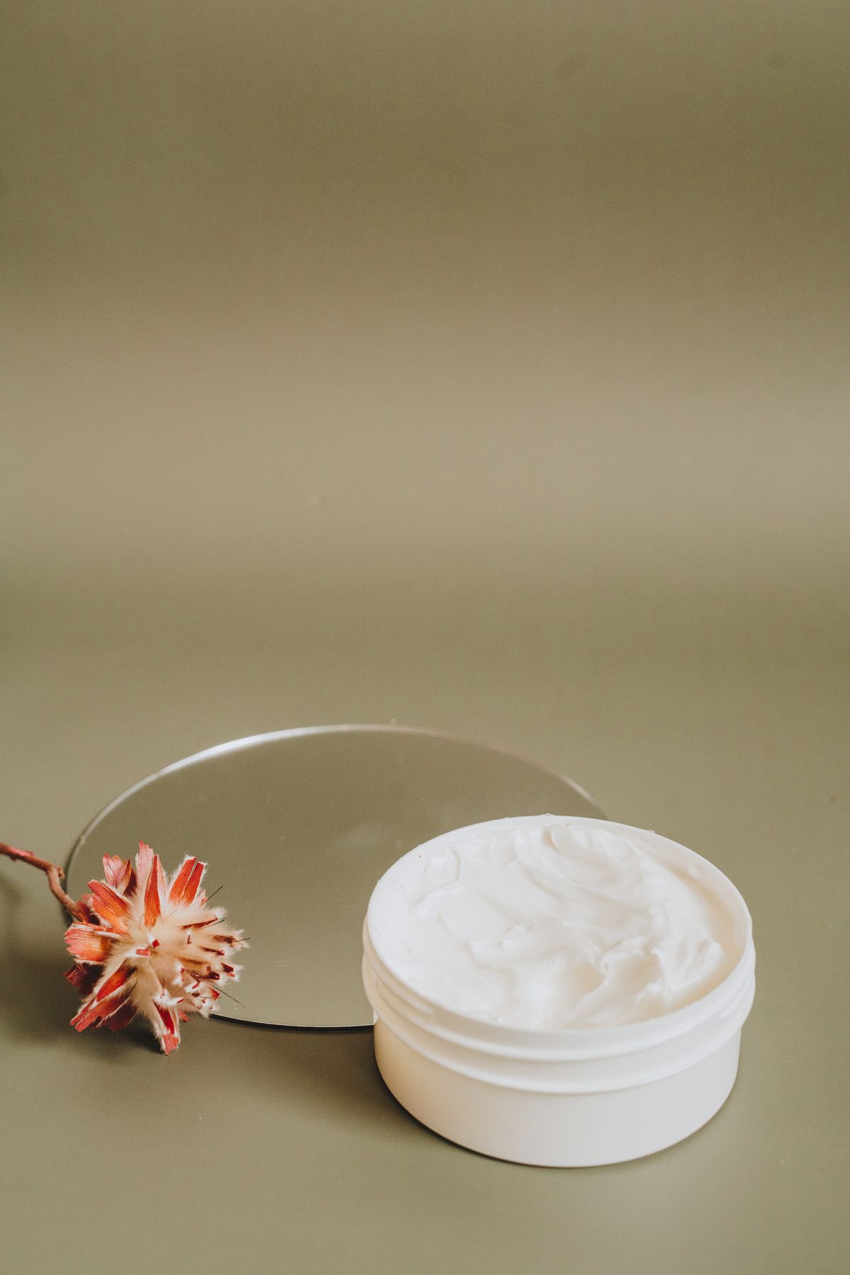 White cream jar with a dried flower on an olive backdrop