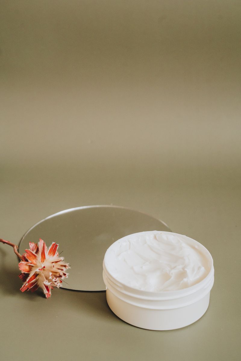 Open jar of face cream on a sage green background