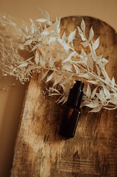 Stylish amber pump bottle on wooden tray with dried foliage in warm tones.
