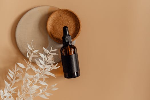 A minimalist skincare bottle with a dropper in a flat lay on a neutral background, surrounded by dried leaves.