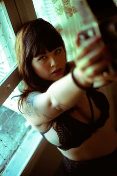 Portrait of a tattooed woman wearing lingerie near a window, featuring a warm, intimate setting.
