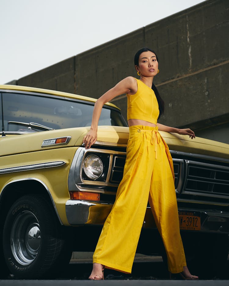 A Woman In A Yellow Outfit Leaning On A Car