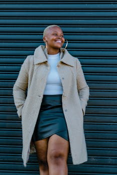 Confident black woman stands against a striped background, showcasing a chic autumn outfit.