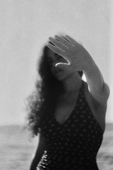 Black and white of young female with curly hair demonstrating control gesture against ocean on sunny day