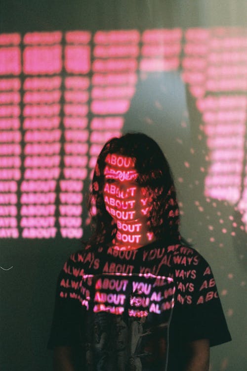 Cool young female in t shirt with letters on face looking at camera in pink light on blurred background