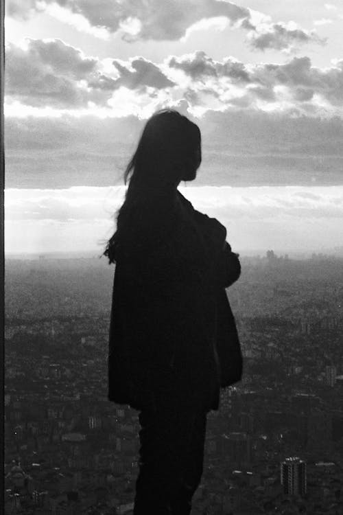 Free Black and white silhouette of unrecognizable female admiring cityscape with residential buildings in city district Stock Photo