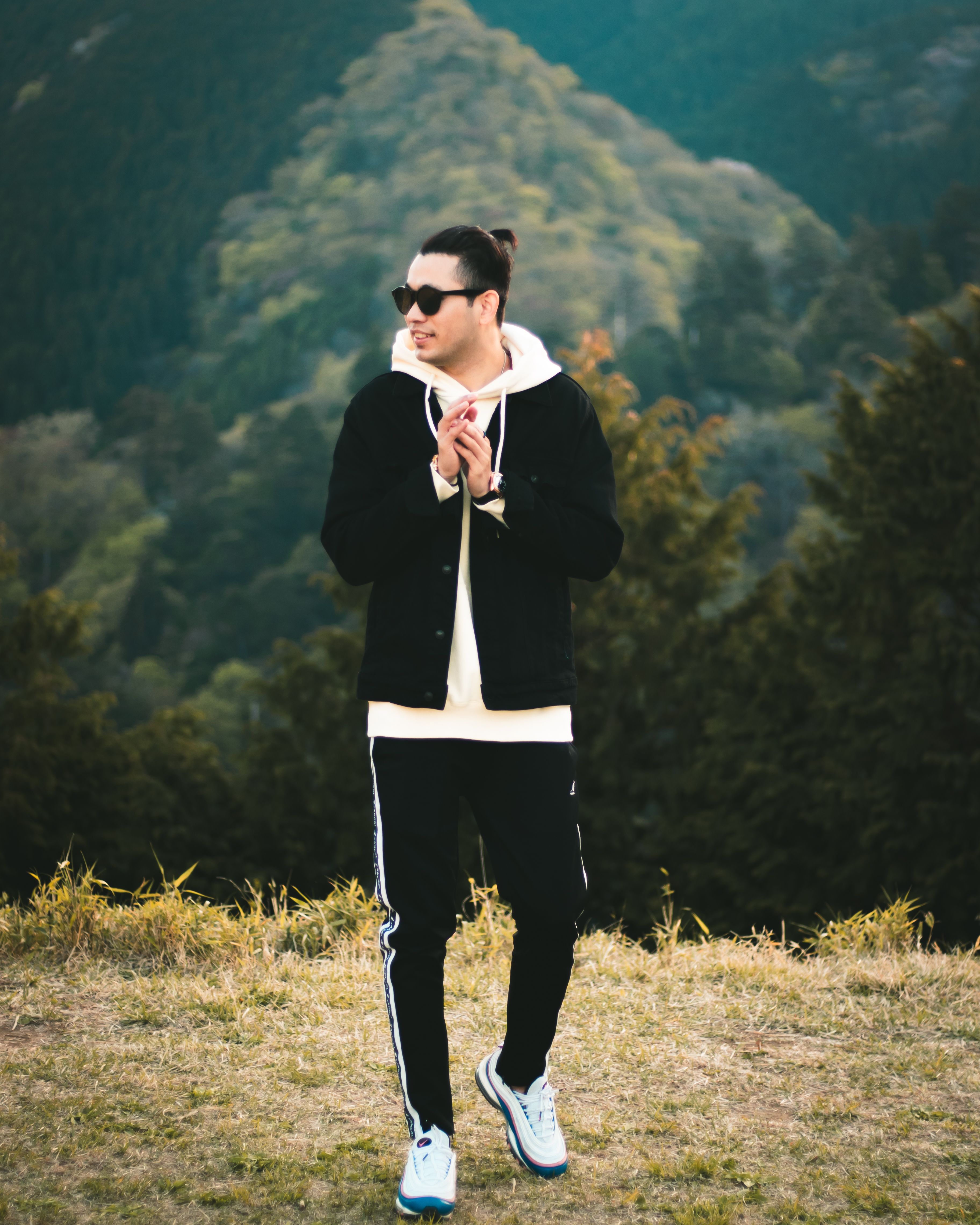 A fashionable man standing outdoors in a stylish casual outfit, surrounded by nature.