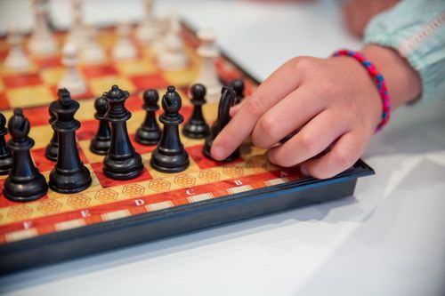 Free A child hand moves a black chess piece on a decorated chessboard, focusing on strategy. Stock Photo