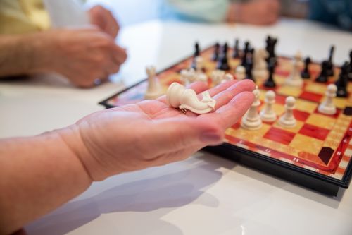 Free A fallen white chess piece rests in a hand with a blurred chessboard background. Stock Photo