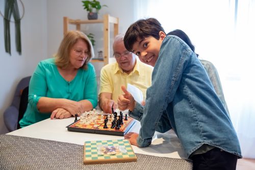Free Grandparents and grandson share a joyful moment playing chess indoors. Stock Photo