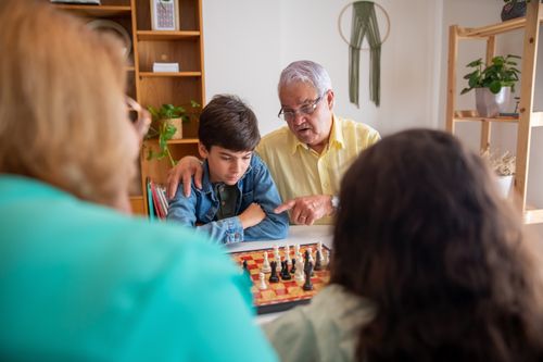 Free A senior man and a young boy focus intently while playing chess together indoors, surrounded by family. Stock Photo