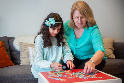 Grandmother and granddaughter enjoying a bonding moment solving a jigsaw puzzle together.