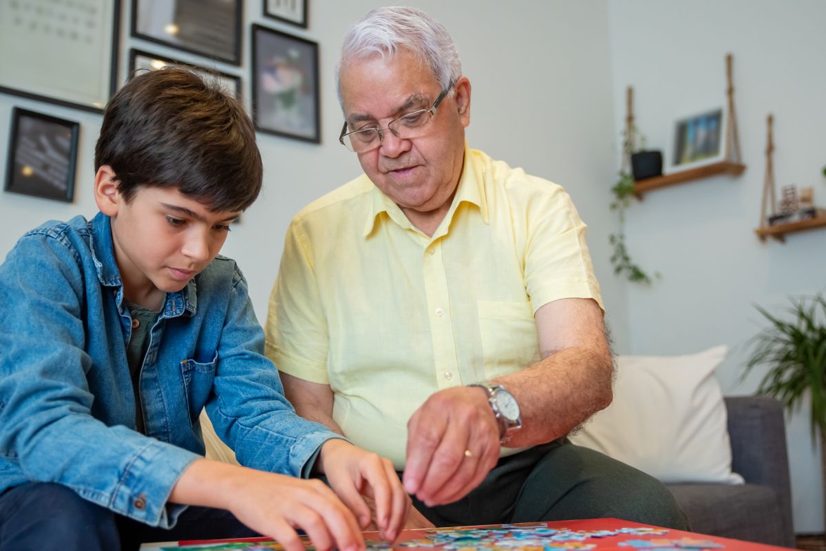 Abuelo haciendo un puzzle con su nieto en el salón de casa, ejercitando la memoria en compañía