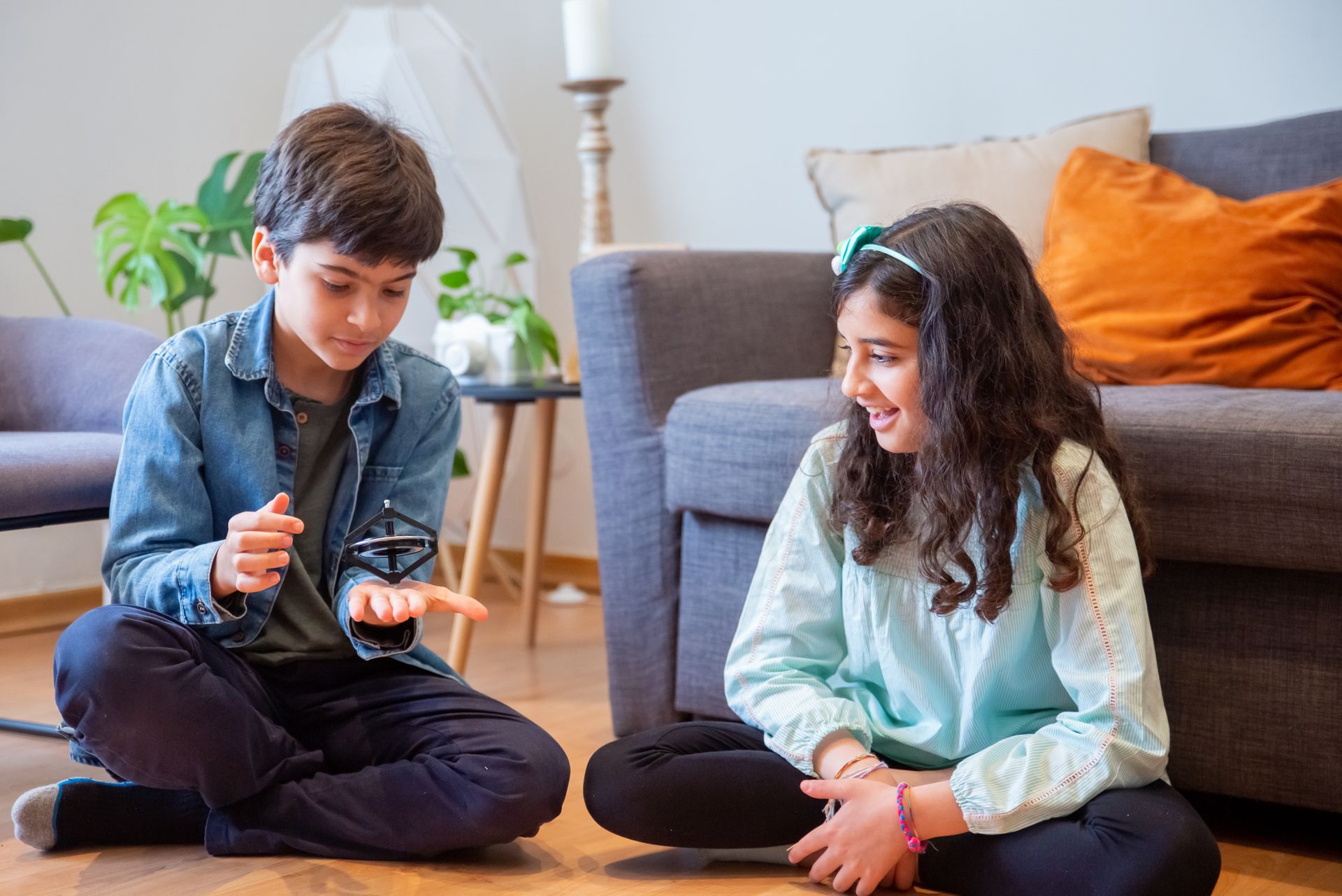 Smiling siblings playing with a spinning top on the floor in a cozy living room.