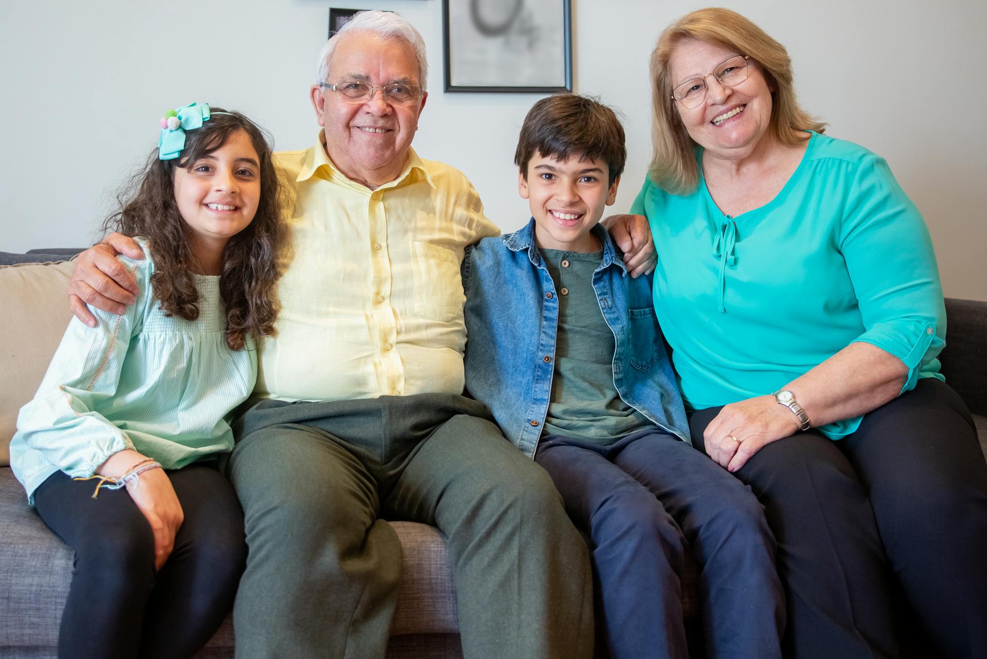 A joyful family portrait with children and grandparents smiling on a sofa indoors.