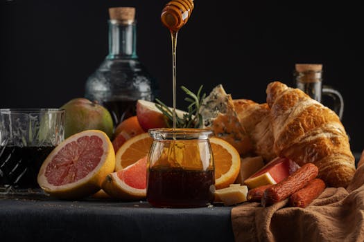 A rustic breakfast setup featuring honey, croissants, fruits, and old-fashioned bottles on a dark background.